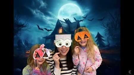 A woman and two children smiling for the camera with Halloween masks they have made.
