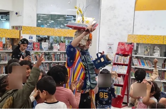 Children enjoying an Octagon Library Tour performance. A man is stood in costume in the middle and children are stood around him participating.