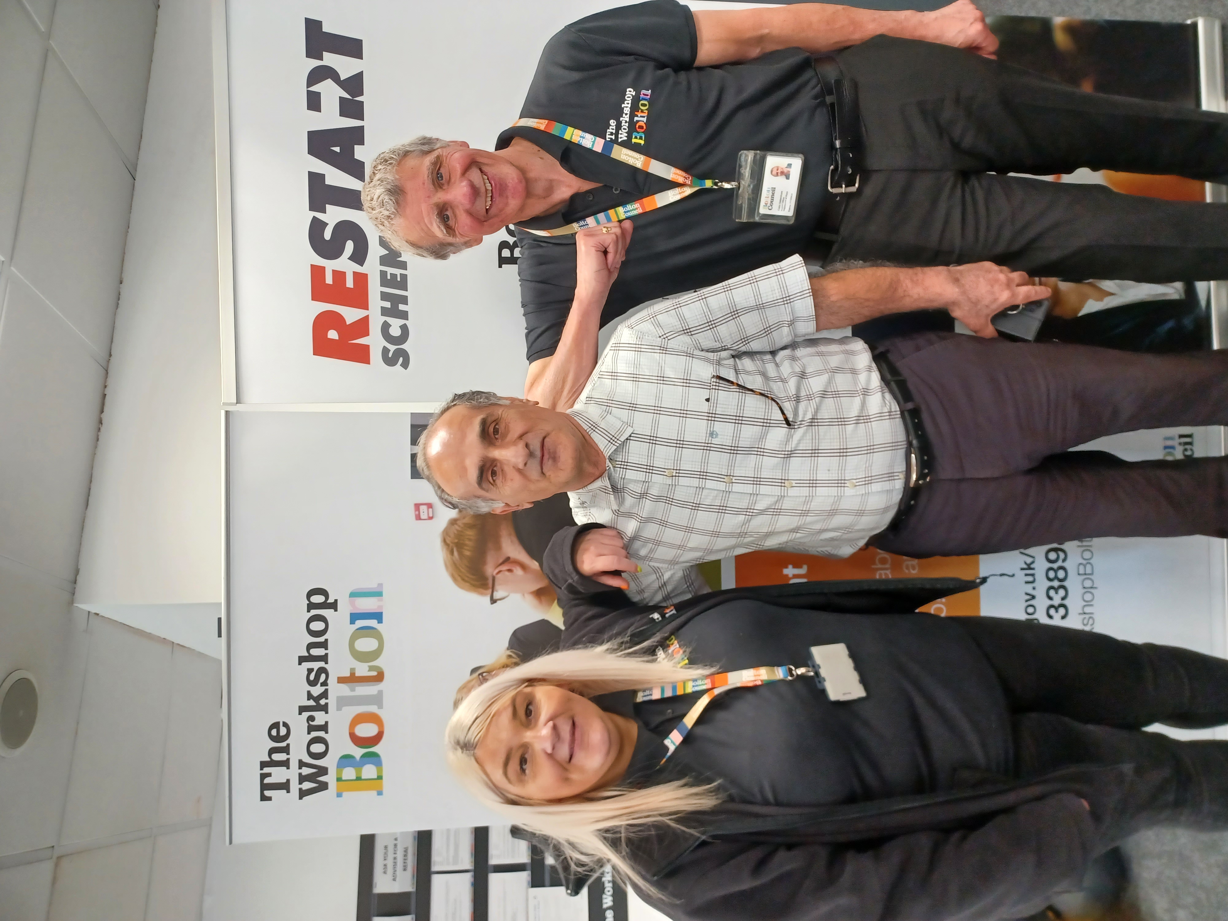 Two smiling Workshop advisors standing on each side of a happy customer with promotional banners behind them.